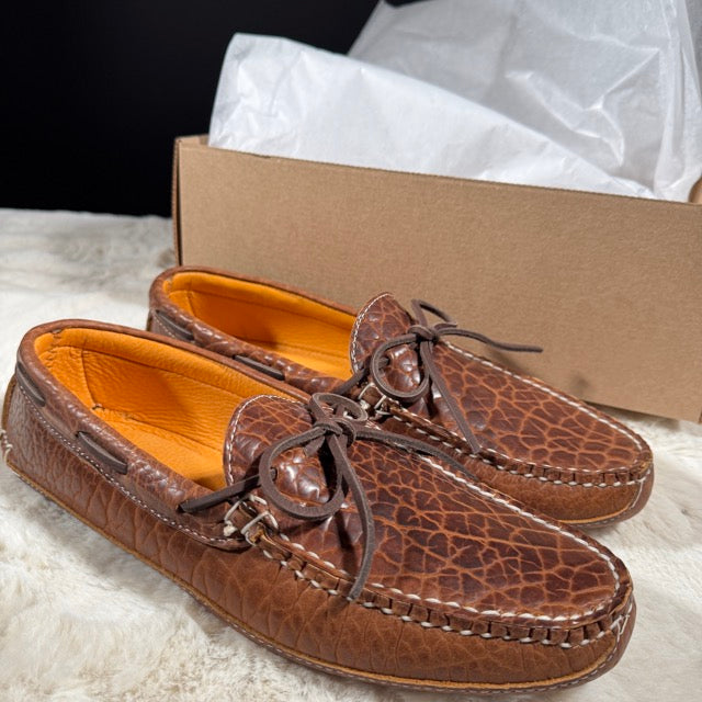 Brown leather shoes with textured finish on a white surface next to a cardboard box.