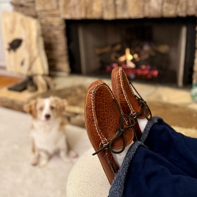 Brown leather shoes with a dog sitting in front of a fireplace.