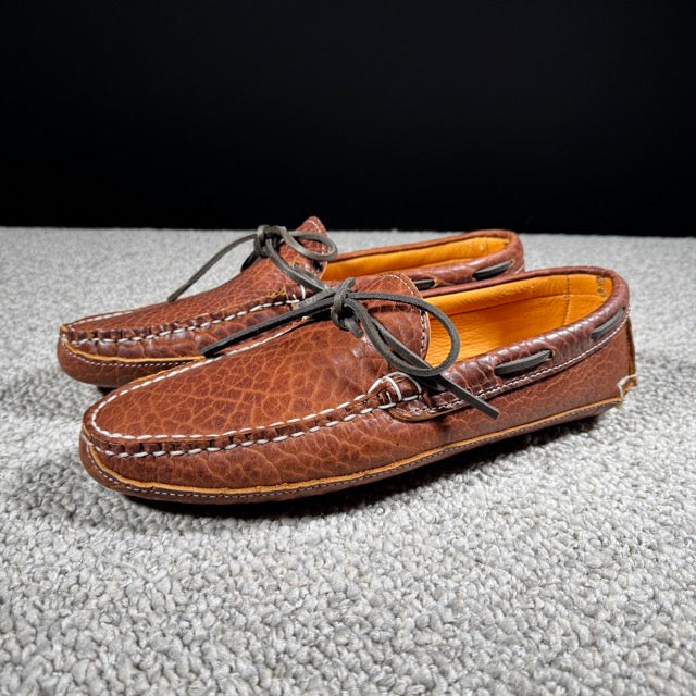 Pair of brown leather loafers on a textured surface with a black background