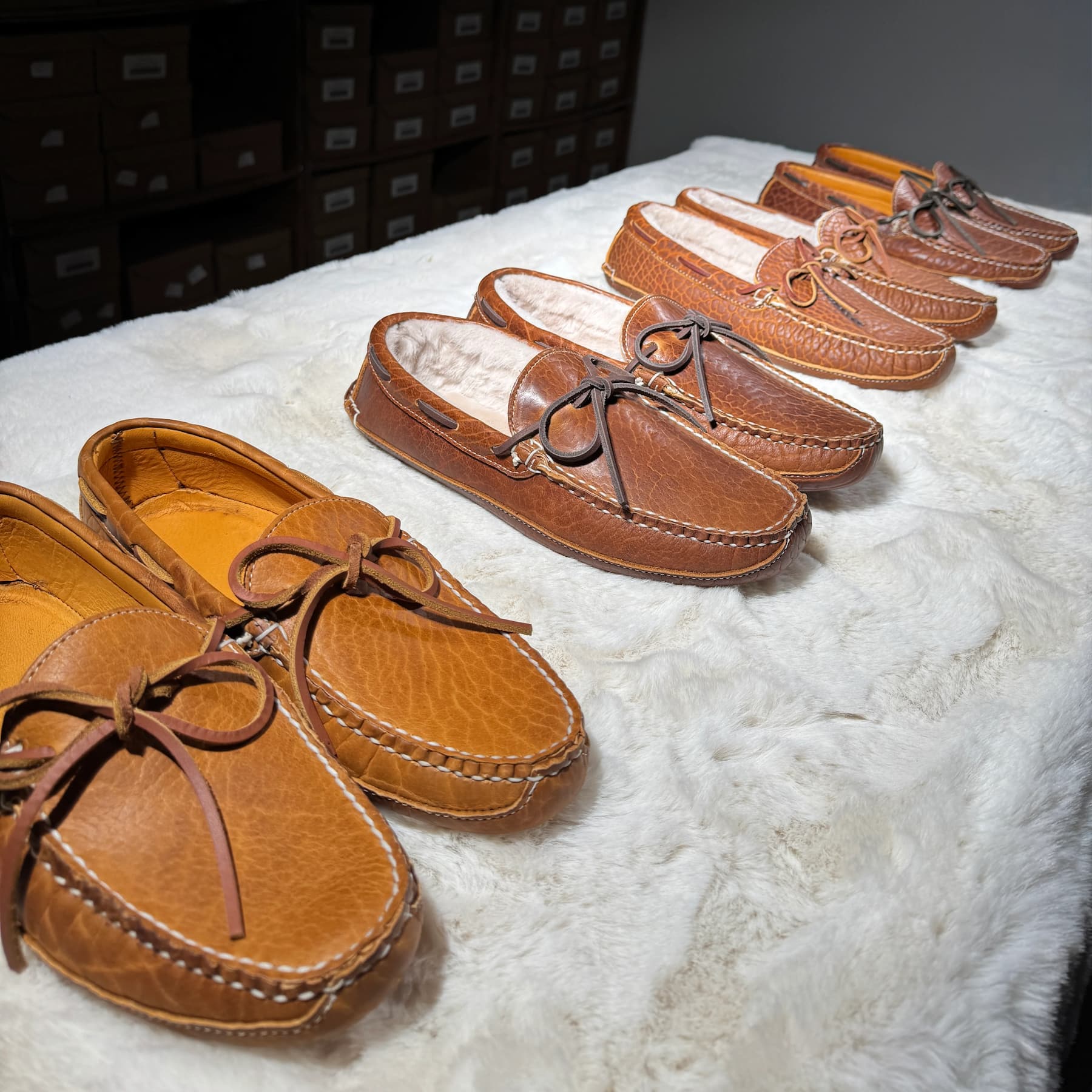 Close-up of handcrafted leather moccasin slippers with shearling lining arranged on a white sheepskin surface.