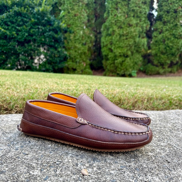 Brown leather loafers on a stone surface with greenery in the background