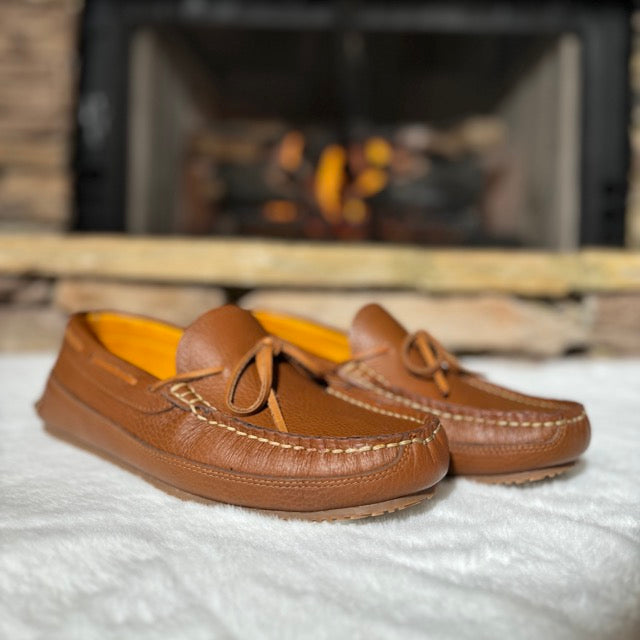 Pair of brown loafers on a textured surface with a fireplace in the background