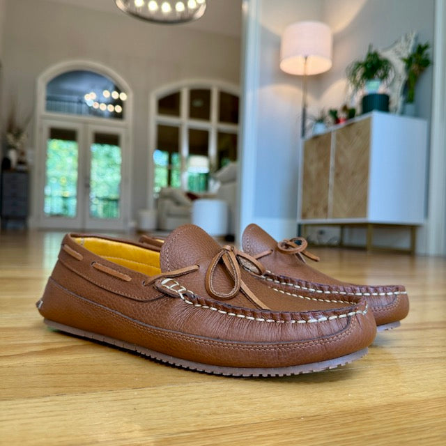 Brown leather moccasins on a wooden floor with a blurred indoor background