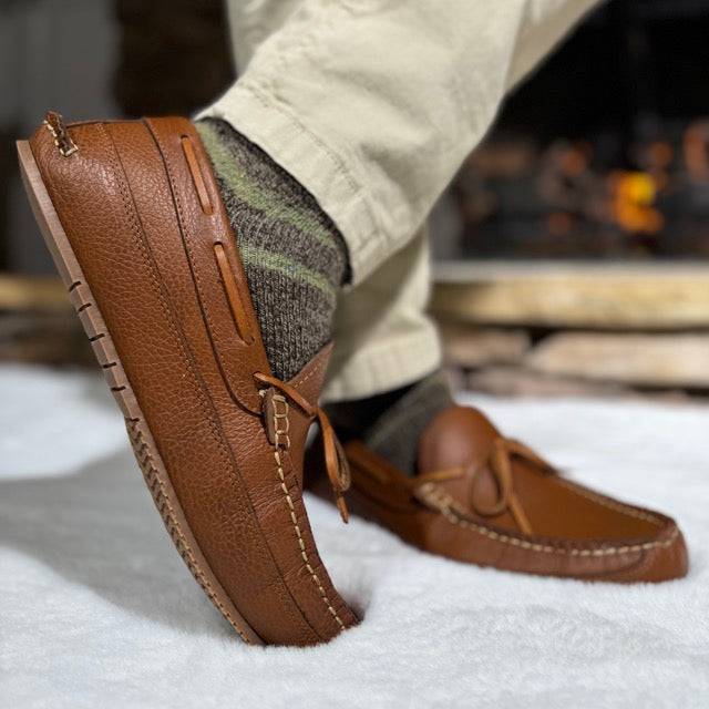 Brown leather shoes worn with a person sitting on a snowy surface.