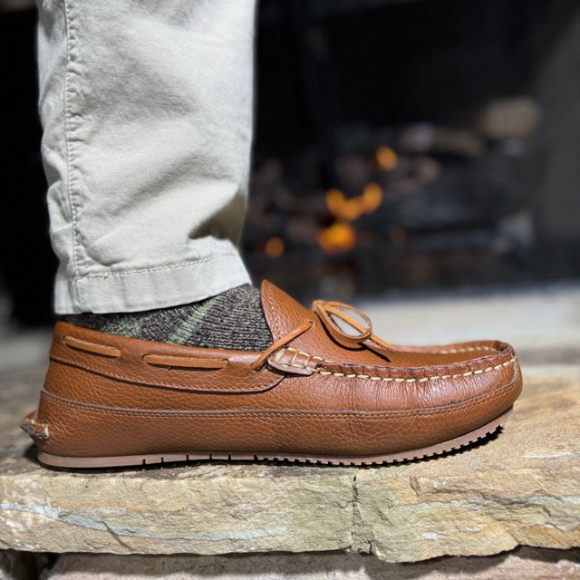 Brown leather loafer worn with light-colored pants on a stone surface.