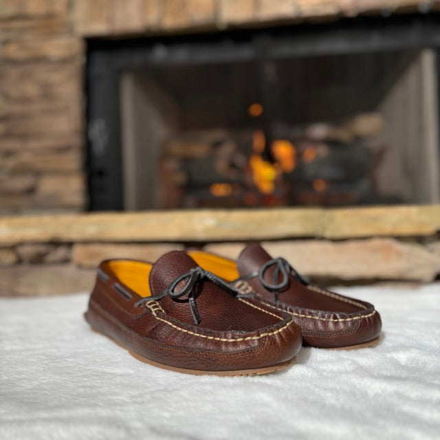 Brown loafers on a white surface with a fireplace in the background
