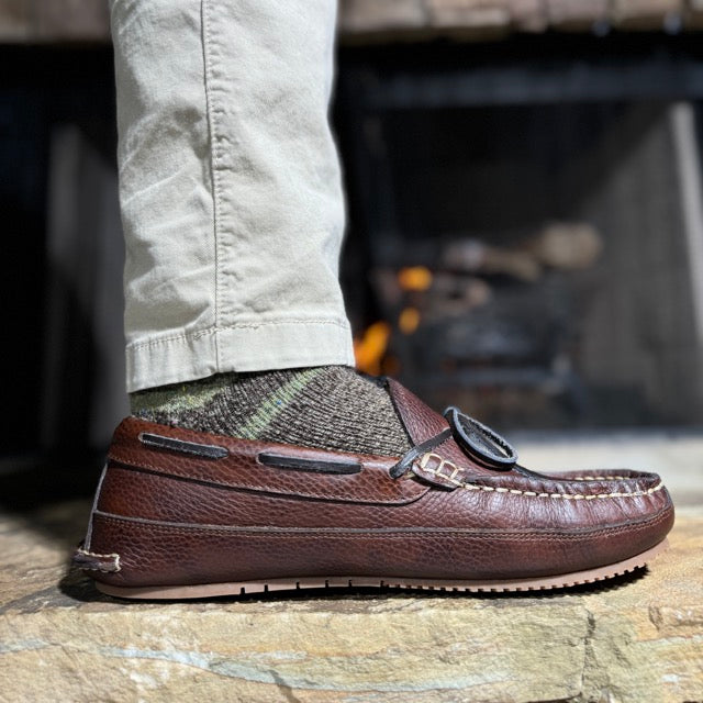 Brown leather loafer shoe worn with light-colored pants on a stone surface.
