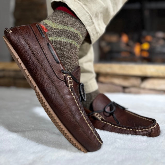 Brown leather loafers worn with striped socks on a blurred indoor background