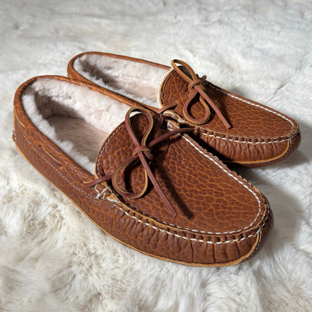 Pair of brown moccasin slippers on a white fluffy surface