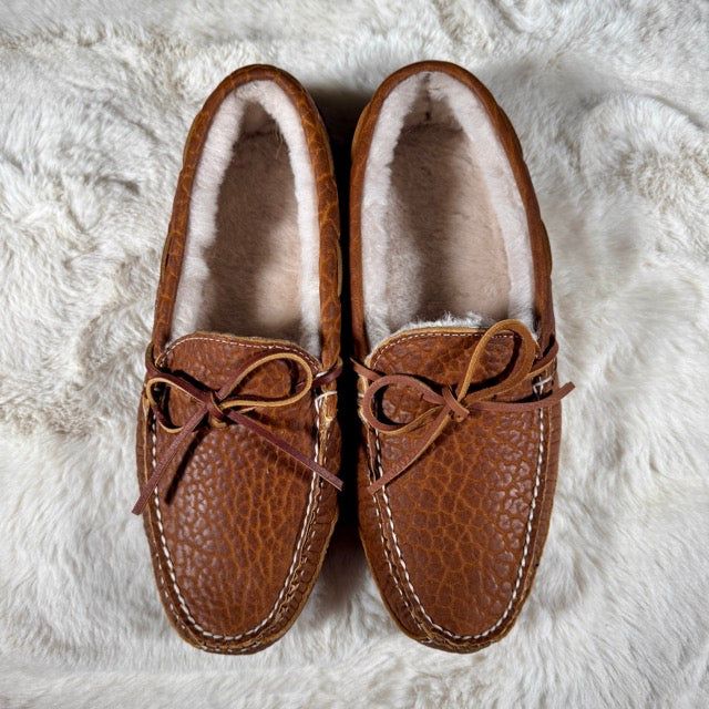 Pair of brown moccasin slippers with fur lining on a white fluffy surface