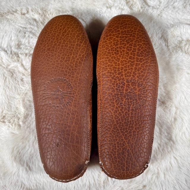 Pair of brown leather shoe inserts on a white fluffy surface