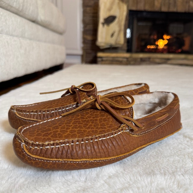 Pair of brown leather moccasins with fur lining on a white surface.