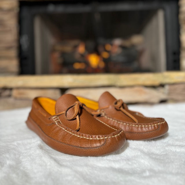 Pair of brown loafers on a white surface with a fireplace in the background