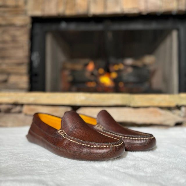 Brown leather loafers on a white surface with a fireplace in the background