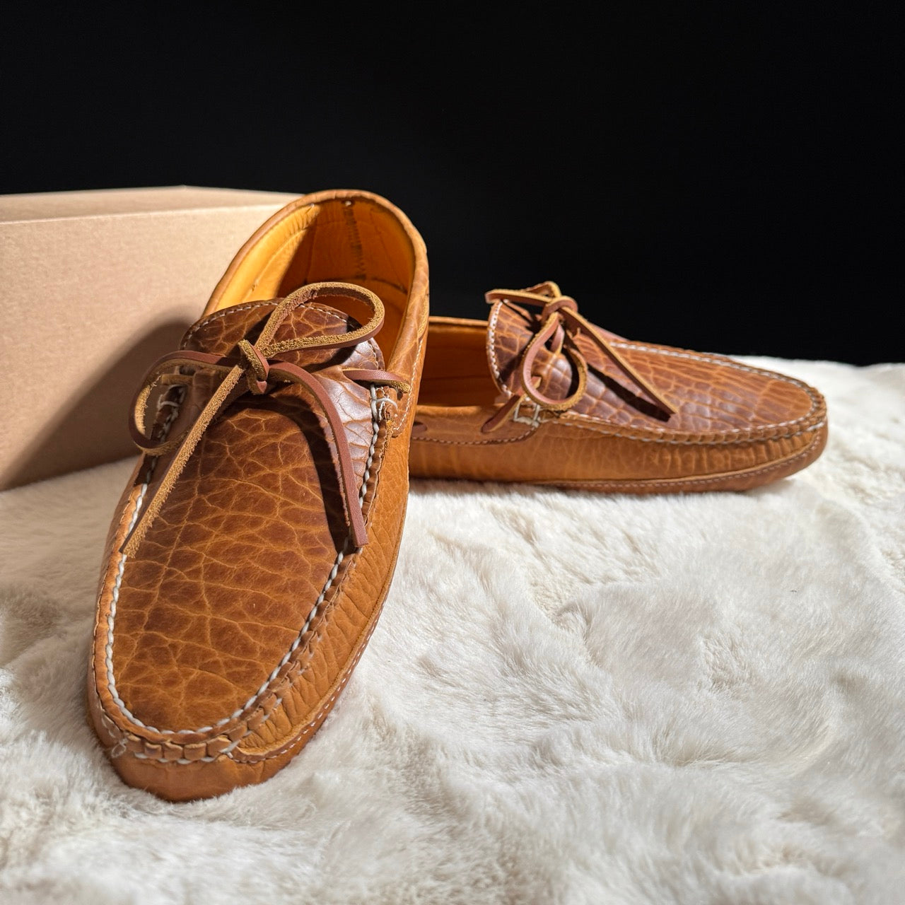 Pair of brown leather moccasins on a white surface with a black background