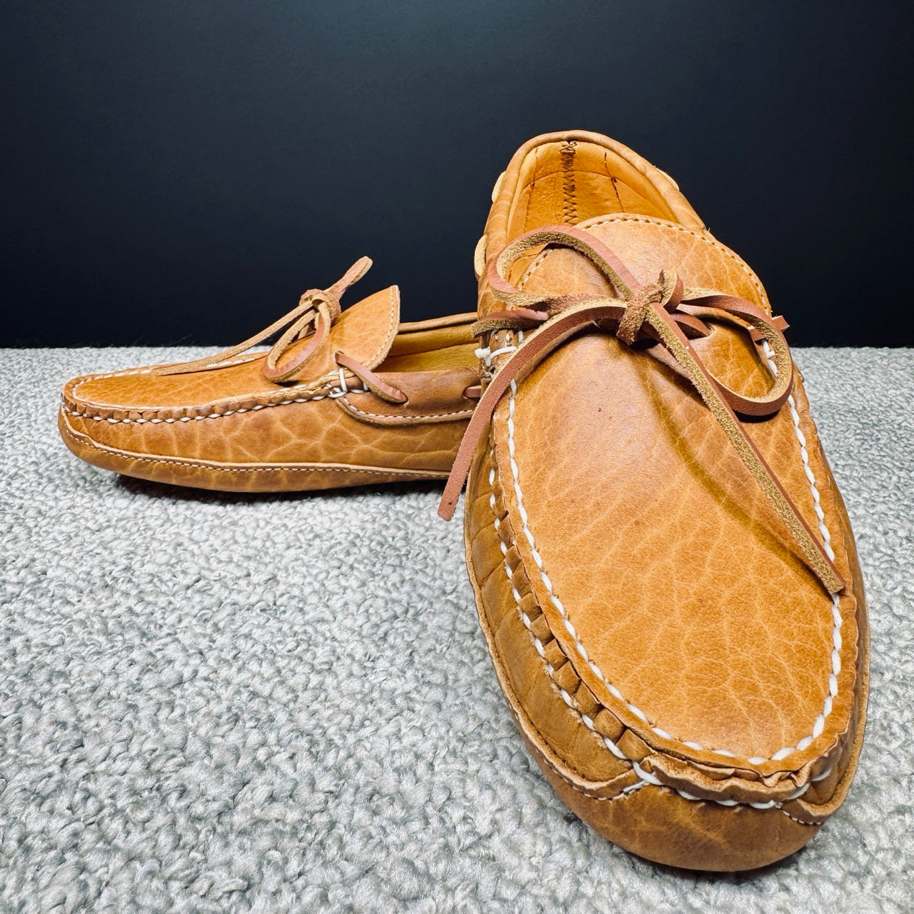 Pair of brown leather moccasins on a textured surface with a dark background