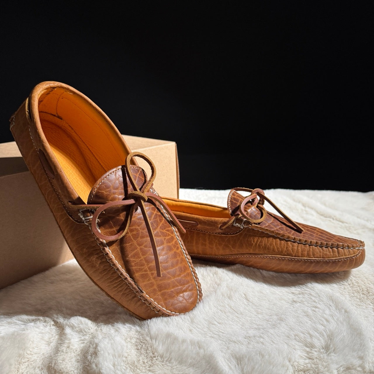 Pair of brown leather moccasins on a white surface with a black background