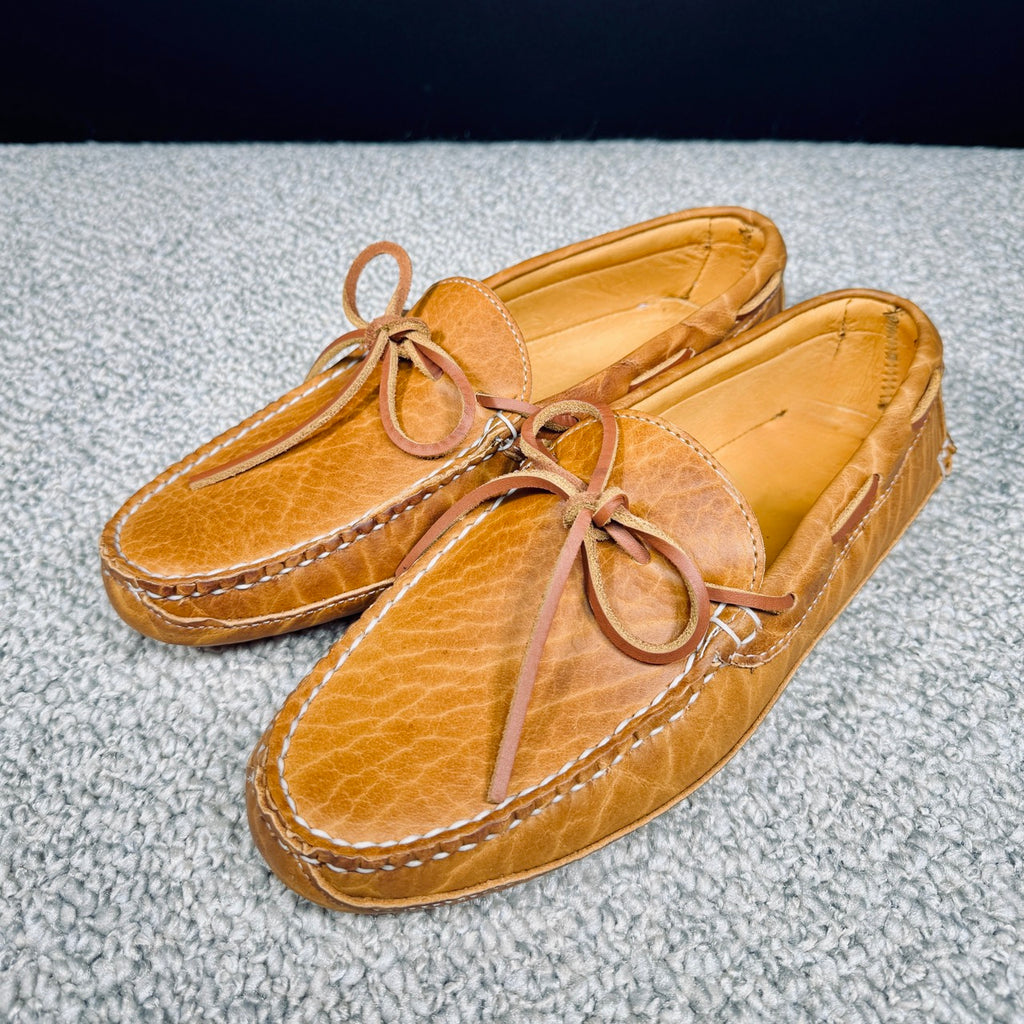 Pair of tan leather moccasins with laces on a textured gray surface.
