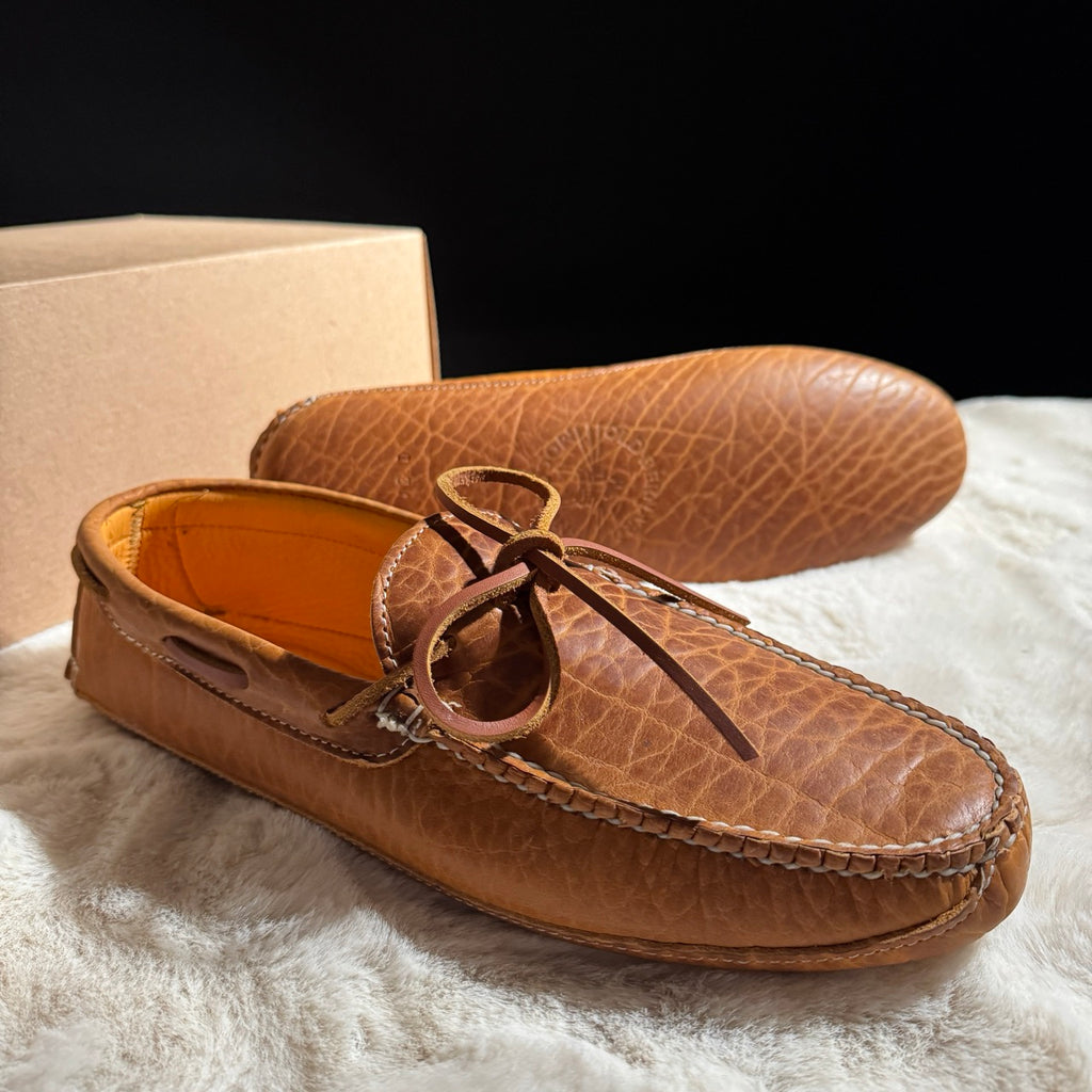 Pair of brown leather moccasins on a textured surface with a black background