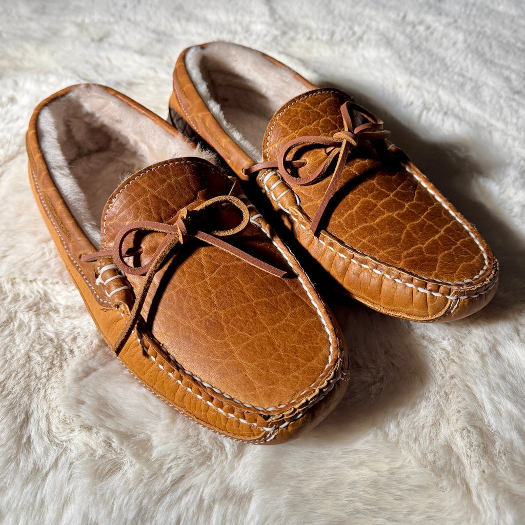 Pair of brown moccasin slippers on a white fluffy surface