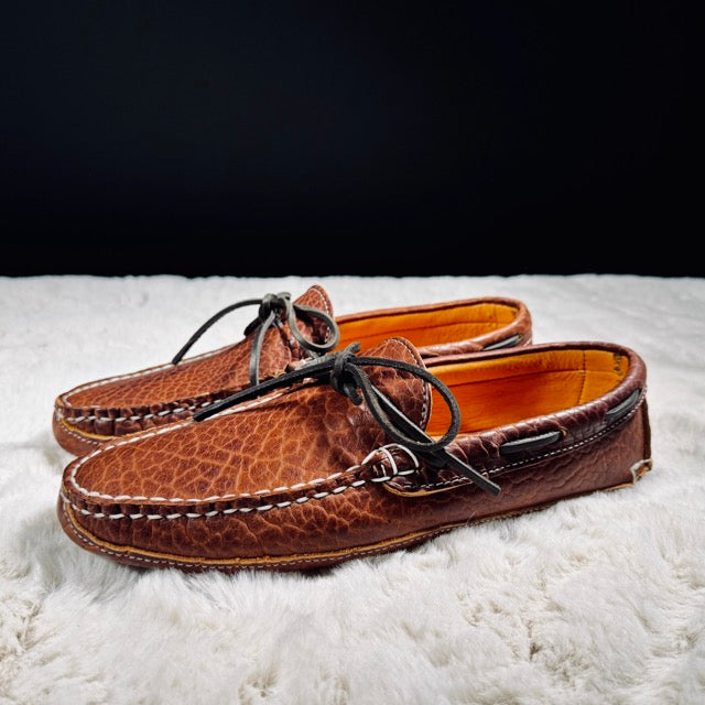 Pair of brown leather moccasins on a white surface with a dark background
