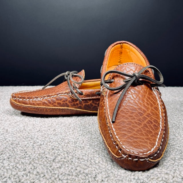 Pair of brown leather moccasins on a textured surface with a dark background