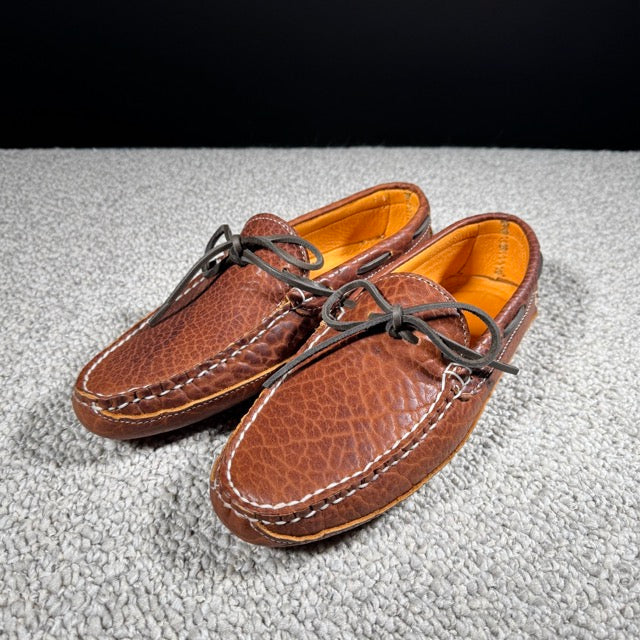 Pair of brown leather shoes with orange lining on a textured gray surface
