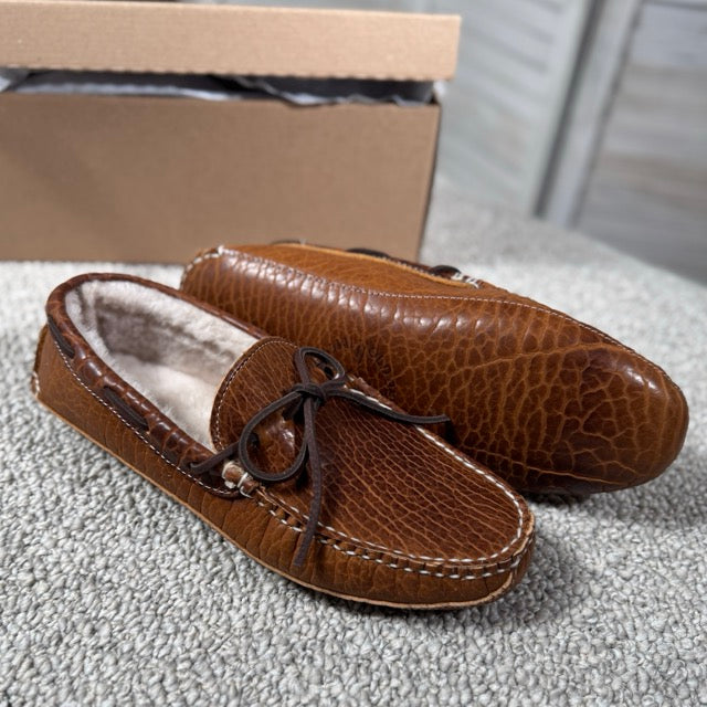 Pair of brown leather moccasins on a textured surface with a cardboard box in the background.