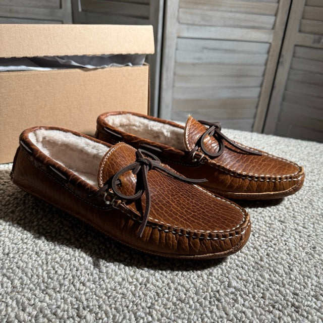Pair of brown leather moccasins with fur lining on a carpeted floor.